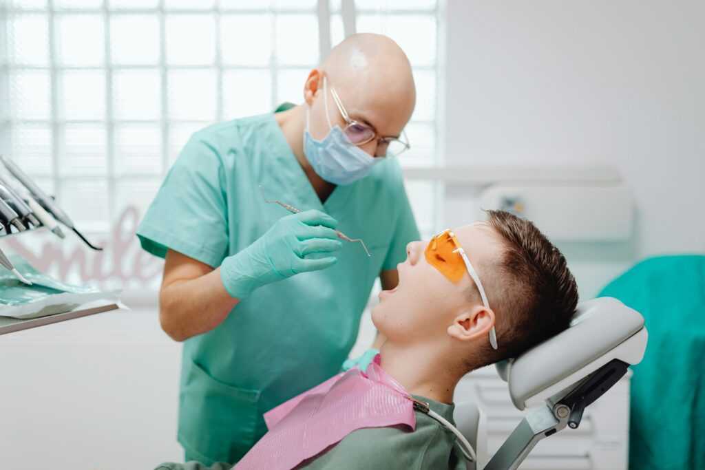A dentist wearing gloves examines a patient sitting in a dental chair, focusing on oral health.